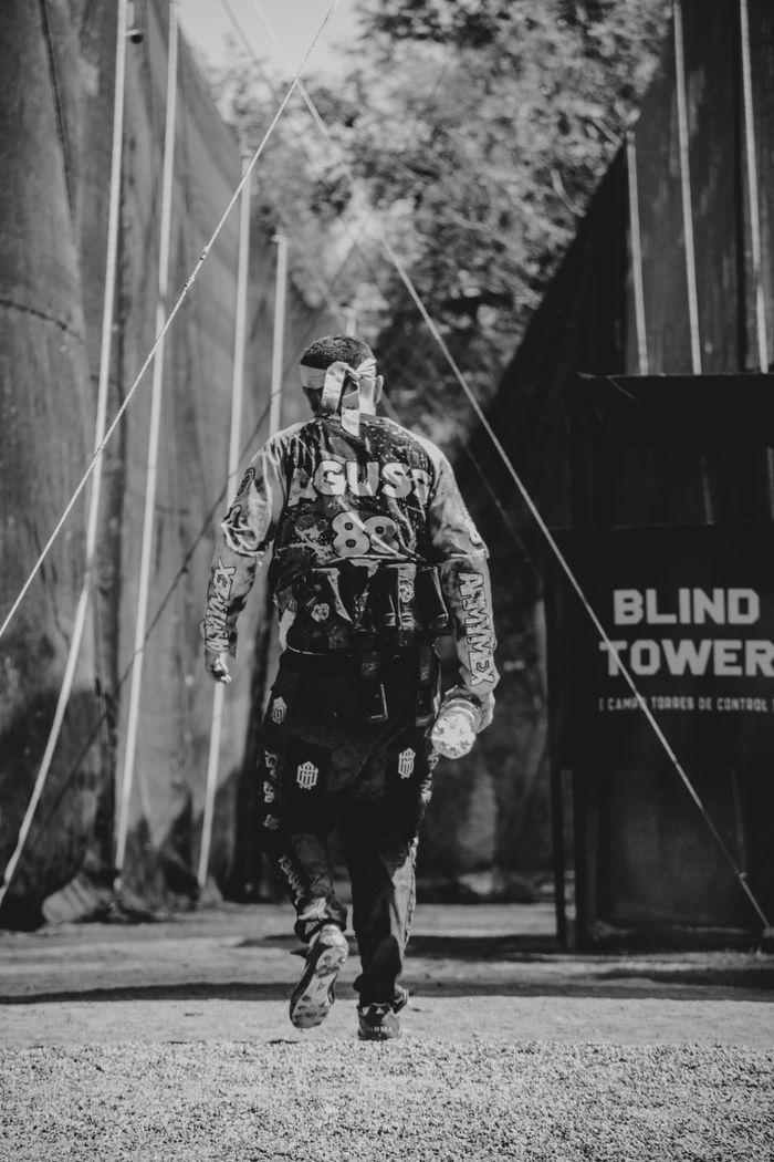 Monochrome image of a paintball player walking towards the tower in a game arena.