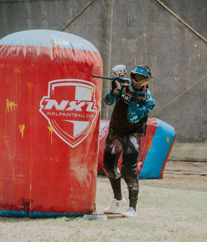 about-us-02 Intense paintball match with player aiming from behind inflatable barrier.