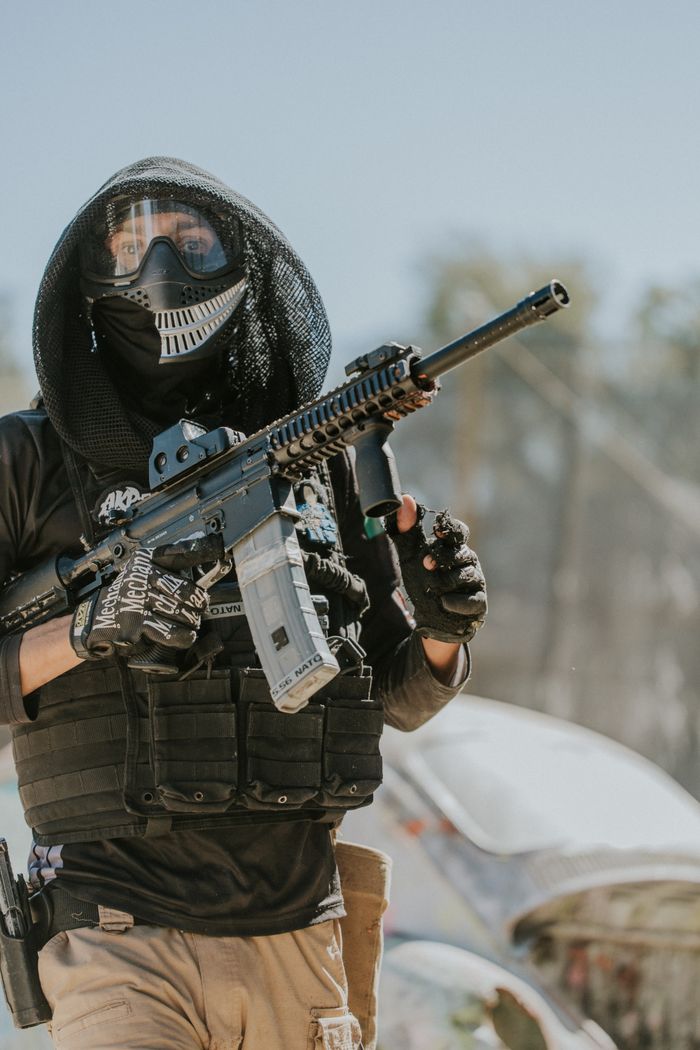 about-us-01 A paintball player dressed in tactical gear and mask holding a paintball rifle outdoors.