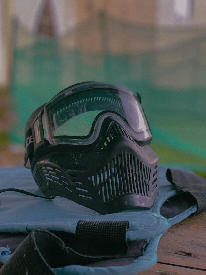 heros-img Black paintball mask on table at outdoor paintball field, ready for action.